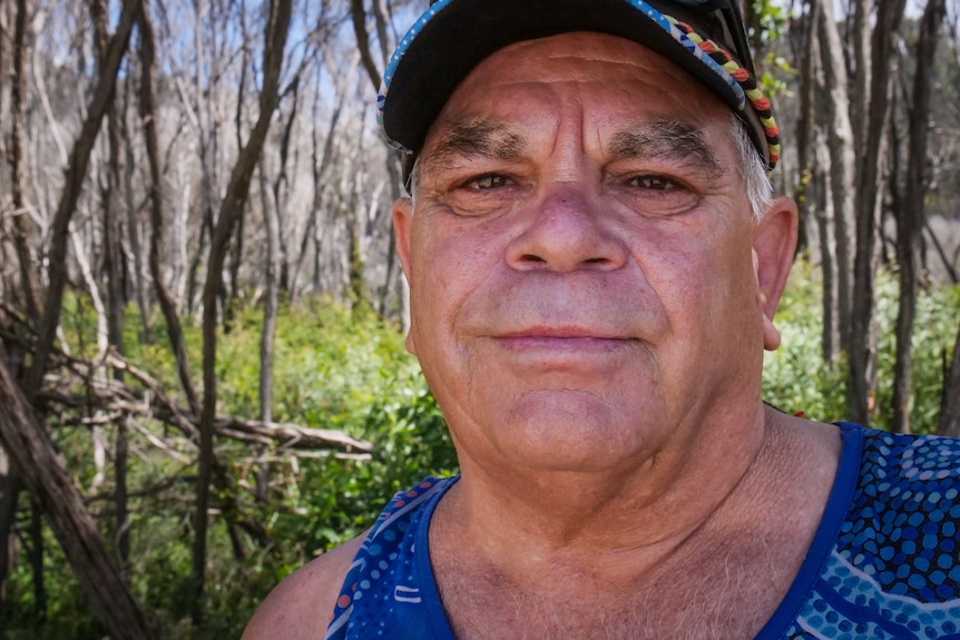 Close up portrait of man looking at camera with bare melaleuca trees in background