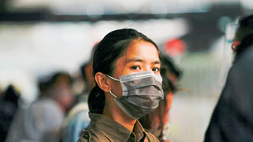 A girl with black hair wears a grey mask and button up shirt.