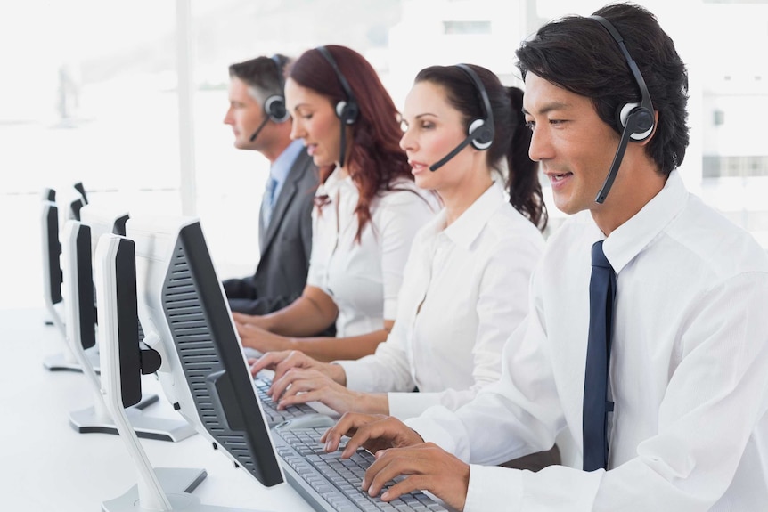 Four call centre staff with headsets on sitting in a row in front of desktop computers talking to clients