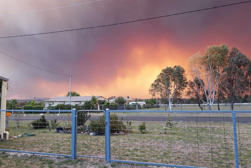 Paddocks with an orange sky and thick smoke behind.