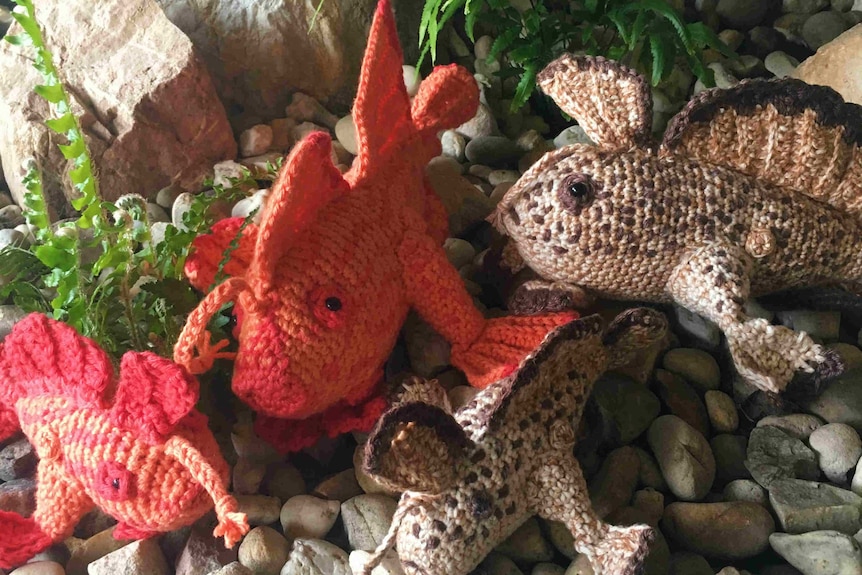 Three crocheted fish sit on a rock