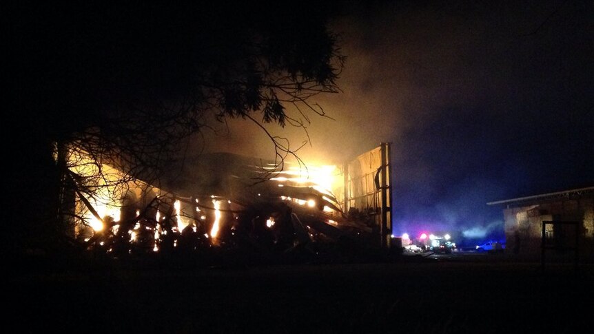 Flames rise from a hay shed with a collapsed roof