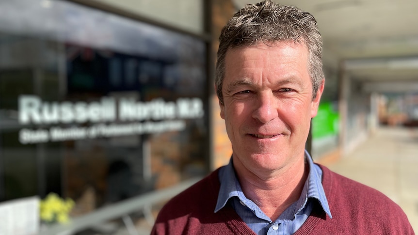 A middle-aged man standing in front of an office window that says Russell Northe MP 