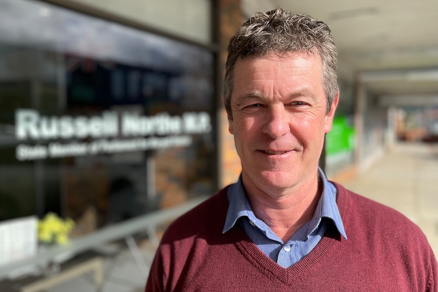 A middle-aged man standing in front of an office window that says Russell Northe MP 