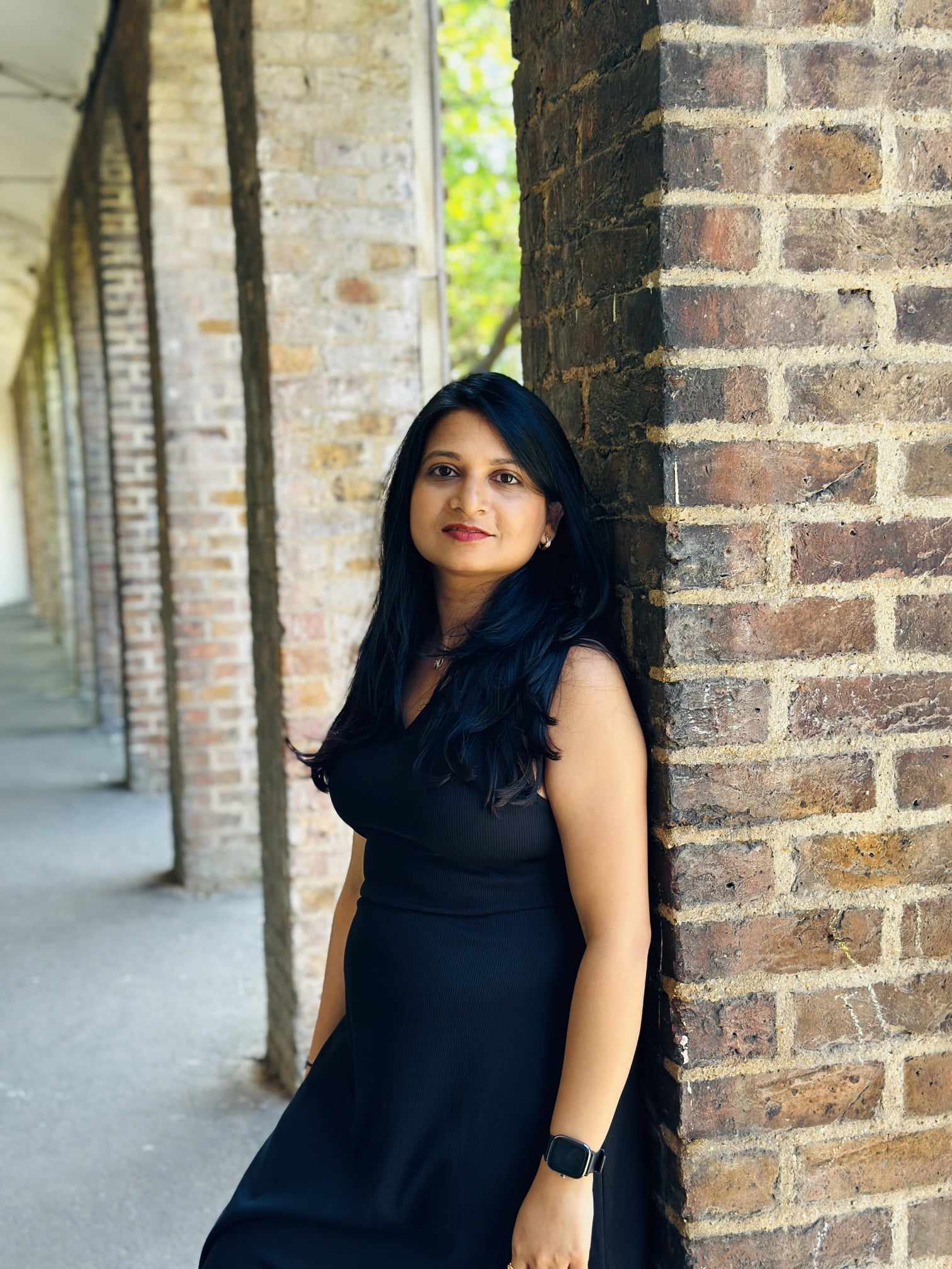 A woman with long black hair leaning against a brick wall