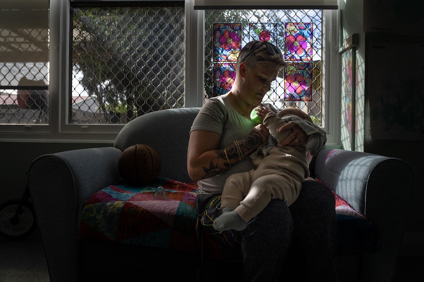 A woman feeds her baby sitting on a couch.
