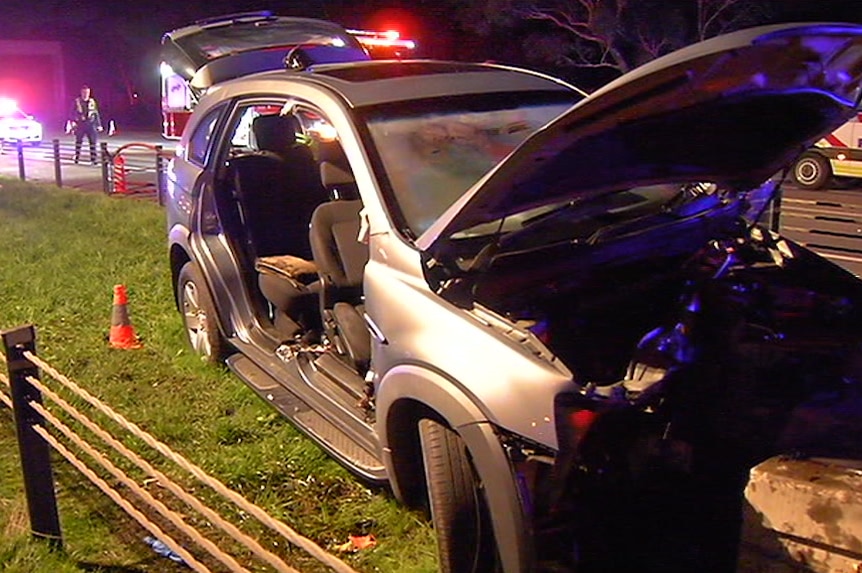 A car with doors removed is illuminated by police sirens on the Monash Freeway's median strip.