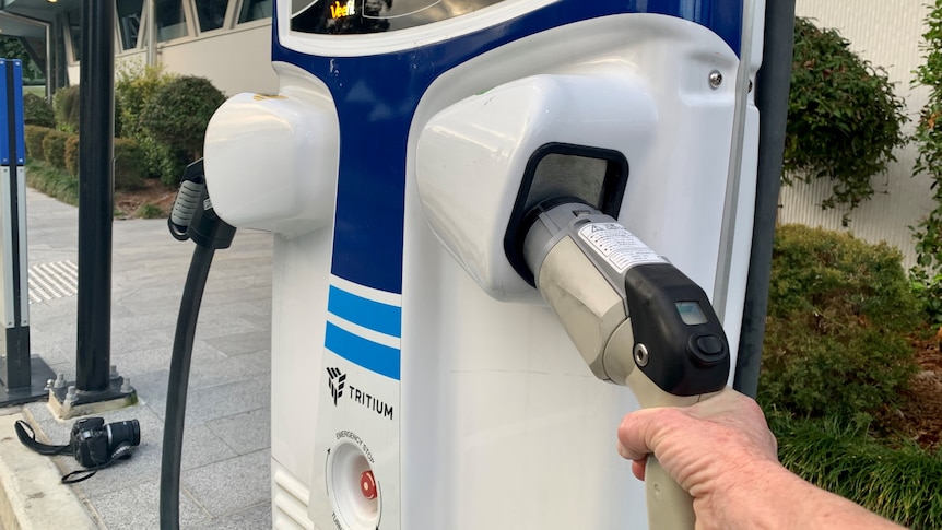 An electric vehicle (EV) charging station with a person's hand on the plug.