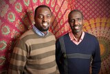 Claude Muco and Mutebutsi Bugegeri stand in front of a large piece of African fabric.