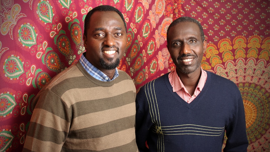 Claude Muco and Mutebutsi Bugegeri stand in front of a large piece of African fabric.