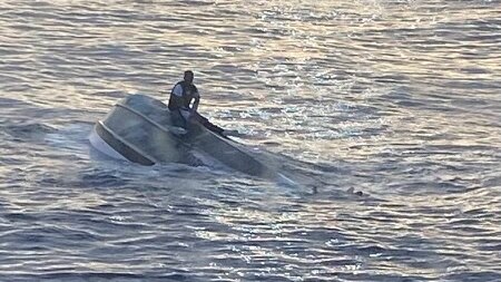 A man sits on top of a capsized boat off the coast of Florida.