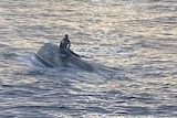 A man sits on top of a capsized boat off the coast of Florida.