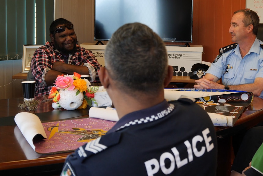 Three men sitting around a table. Two of them are police officers and one of them is a participant in the justice program. 