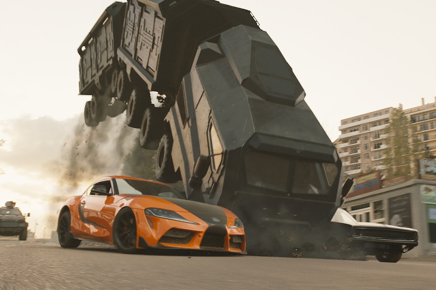 Two cars flanking a truck cause it to crash, its back wheels in midair, in Fast and Furious 9