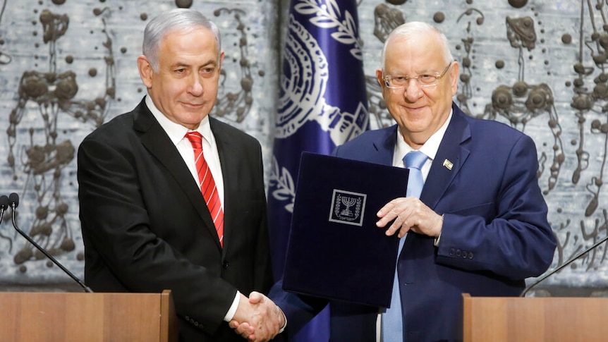 Reuven Rivlin wears a navy suit as he shakes hands with Benjamin Netanyahu who wears a black suit with a red tie.