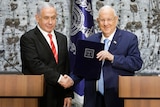 Reuven Rivlin wears a navy suit as he shakes hands with Benjamin Netanyahu who wears a black suit with a red tie.