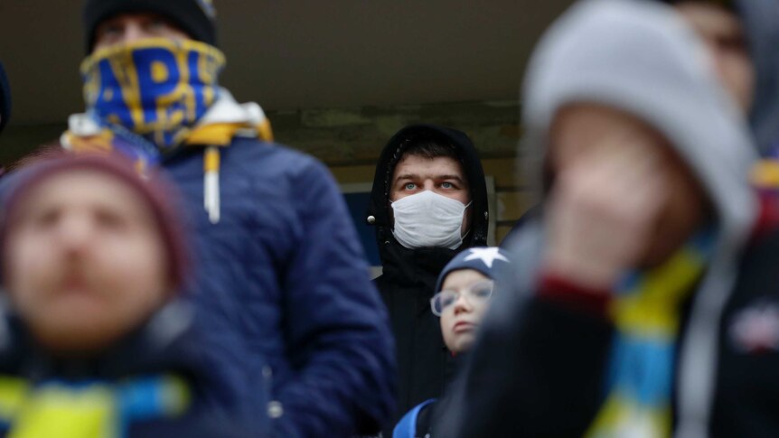 A man wears a surgical mask and a black hooded coat