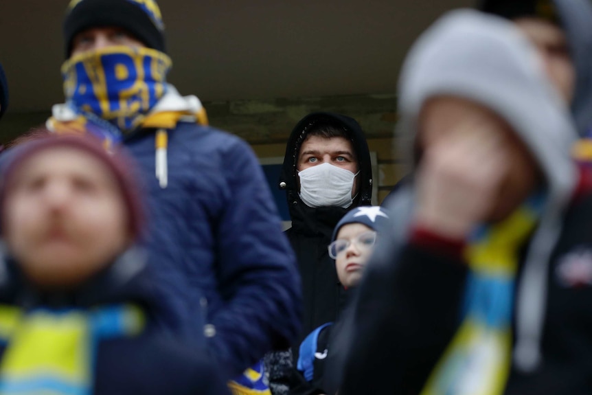 A man wears a surgical mask and a black hooded coat