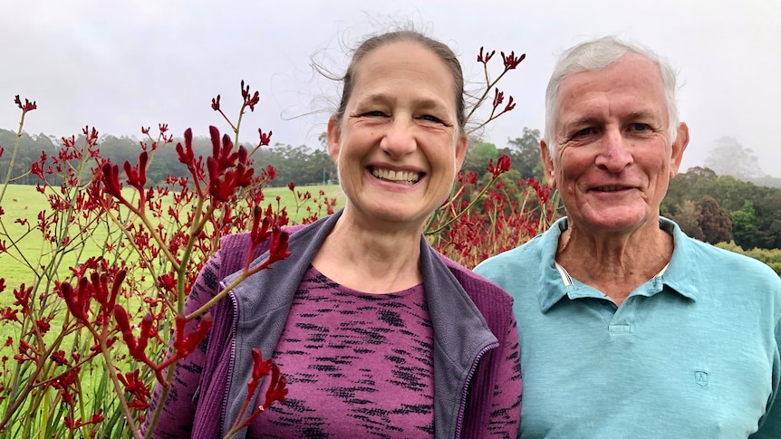 A couple smiling with tall red kangaroo paw flowers behind them.