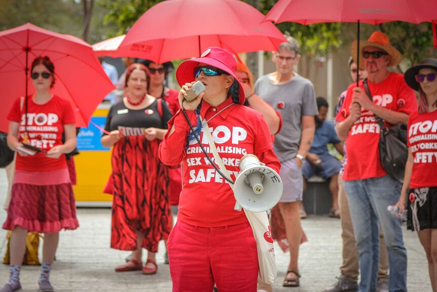 A woman with a red shirt and loudspeaker addresses a rally.