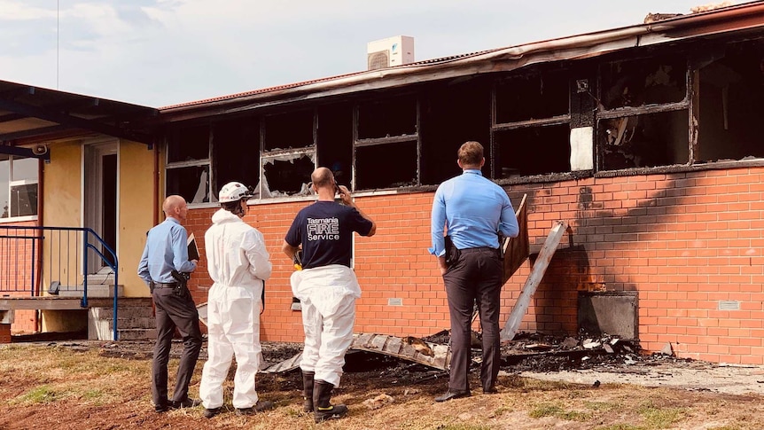 Police and firemen looking at the burnt out windows of a primary school.
