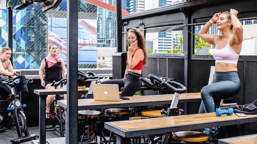 Four women smile as they sit on exercise bikes in a bar.