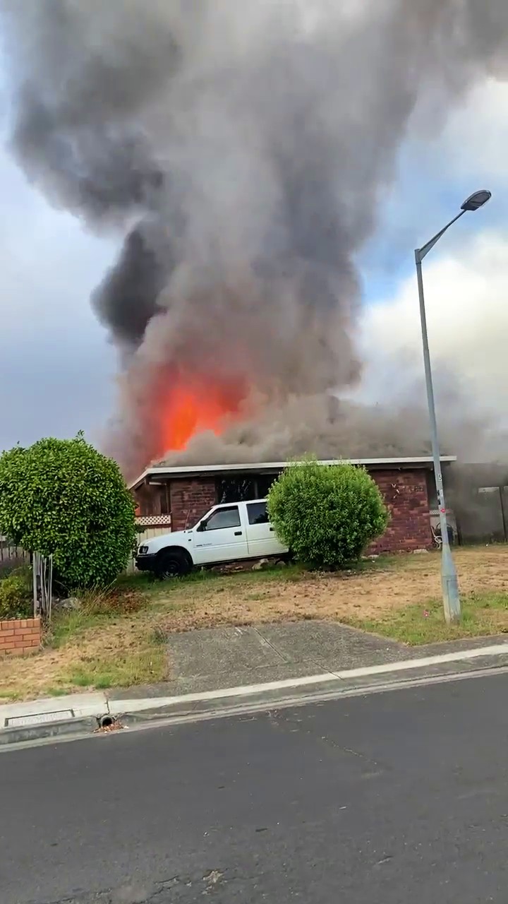 A single-storey home on fire with flames and smoke rising from the roof with a white car parked outside.