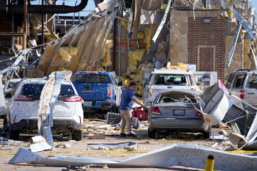 A man looks at a damaged car after a tornado hit the day before