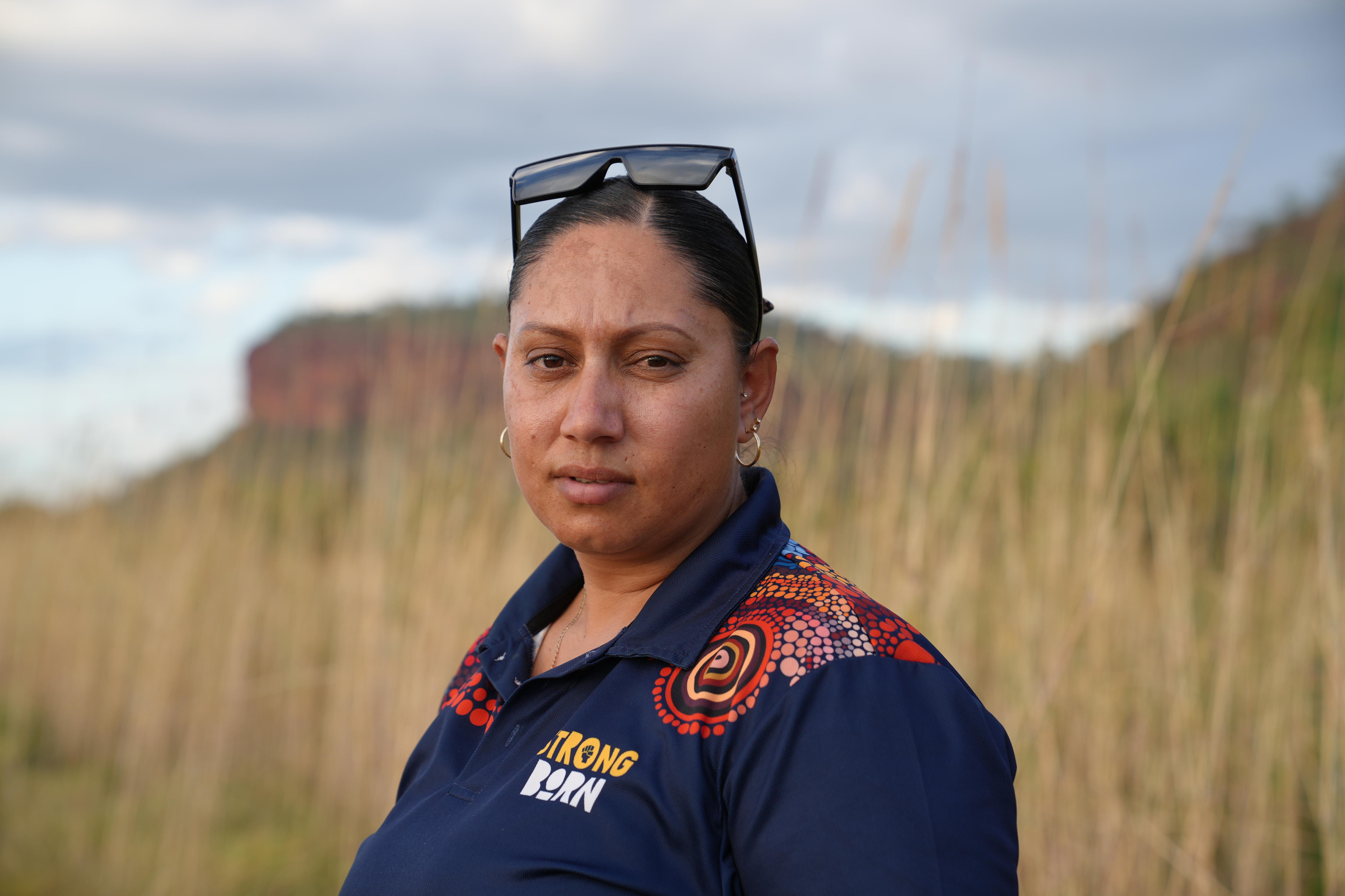 Una mujer que usa una camisa con arte de punto se encuentra frente a la hierba larga.
