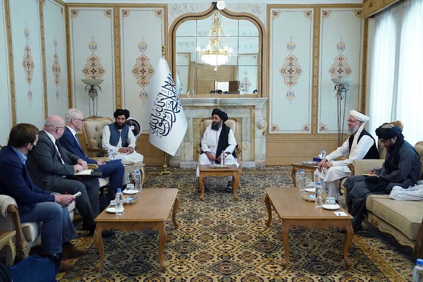 Men in suits sit with Taliban men in traditional Afghan dress.