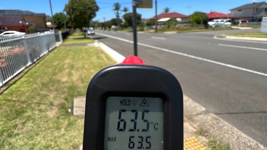 A device reading the number 63.5 degrees Celsius with a bus stop pole next to a wide road