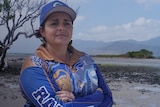 A woman wearing a blue cap and shirt stands in front of wetlands.
