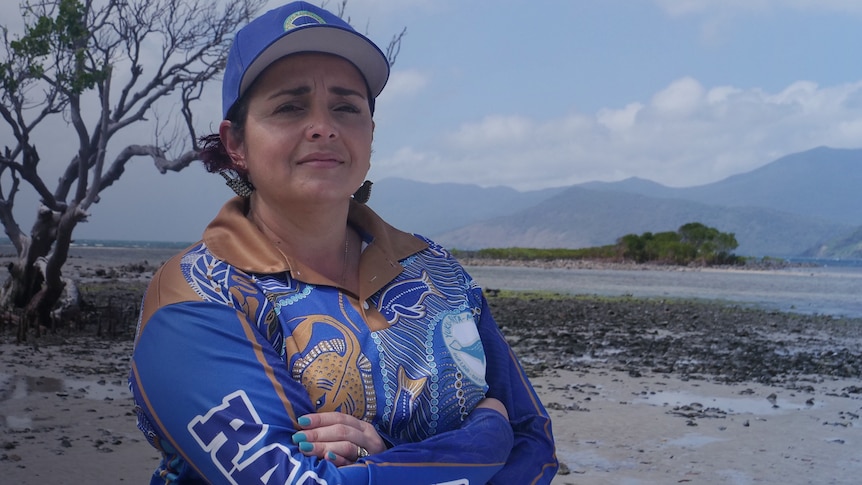 A woman wearing a blue cap and shirt stands in front of wetlands.