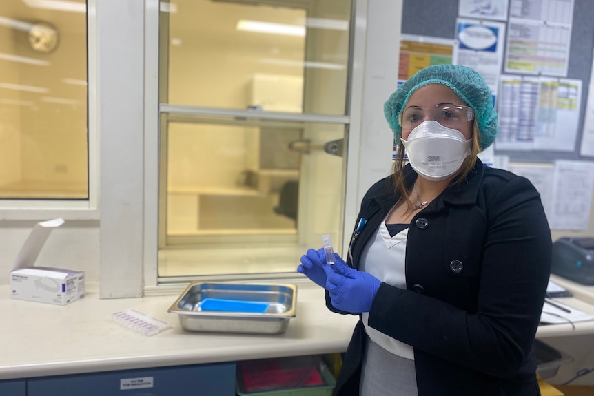 A woman in PPE holding up a small vial in a laboratory.