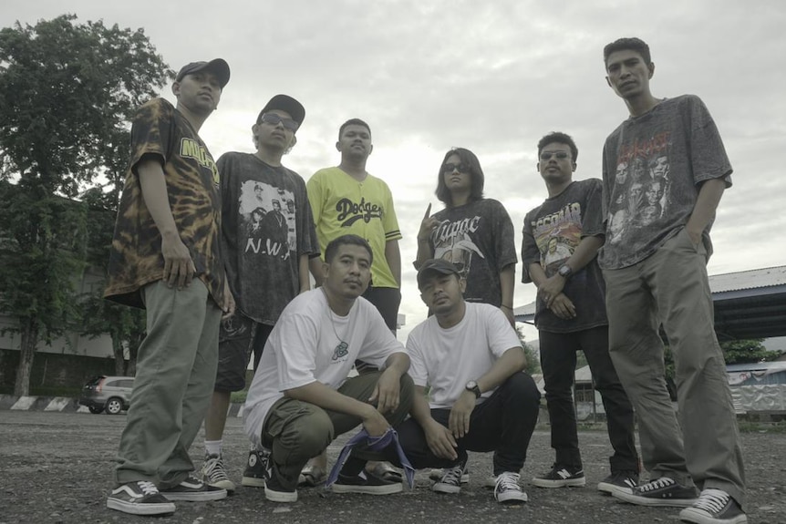 Six people, one of them women, stand facing the camera, in front of them two men are crouching facing the camera.