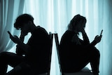 A silhouette photograph of two teenagers, back to back in chairs, on their smartphones