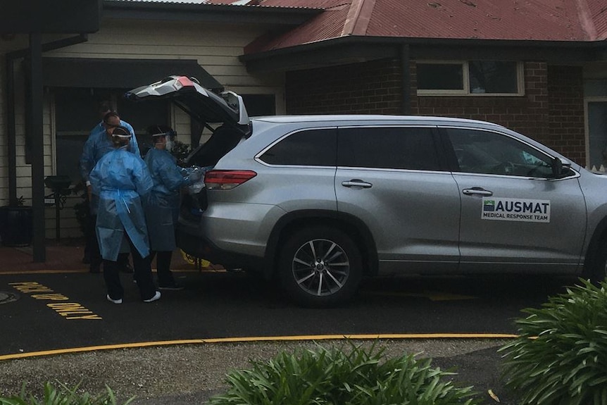 People in protective suits remove gear from the back of a car