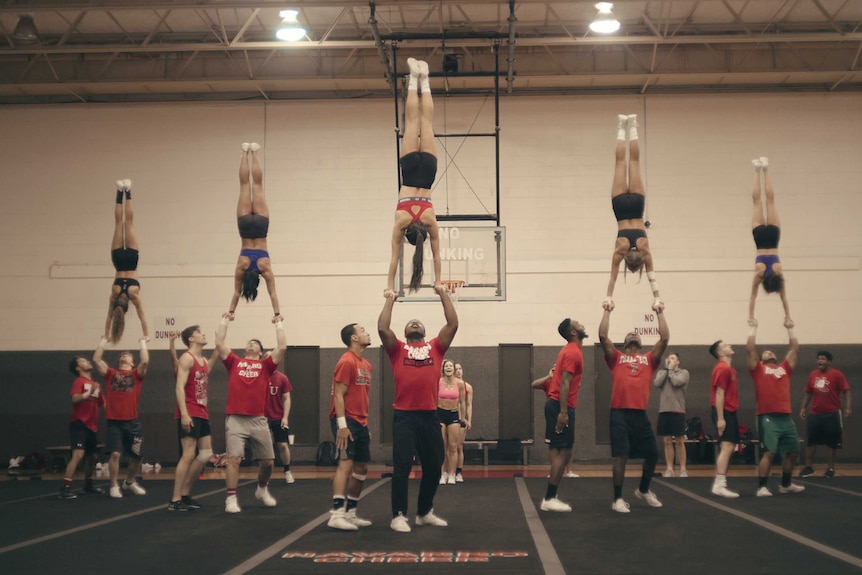 Five cheerleaders performing handstands balancing on other team members' hands, in story about cheerleading and Netflix Cheer.