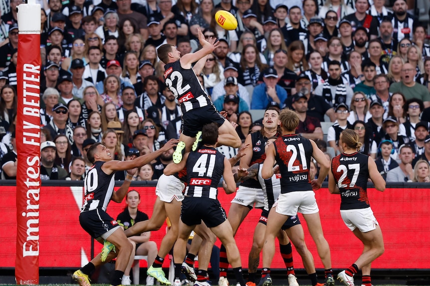 A Collingwood player jumps on top of a pack of players to go for a mark.