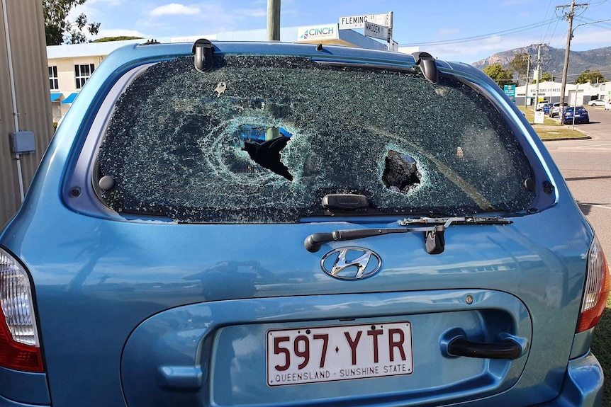 A blue car with a shattered back windscreen parked on a street