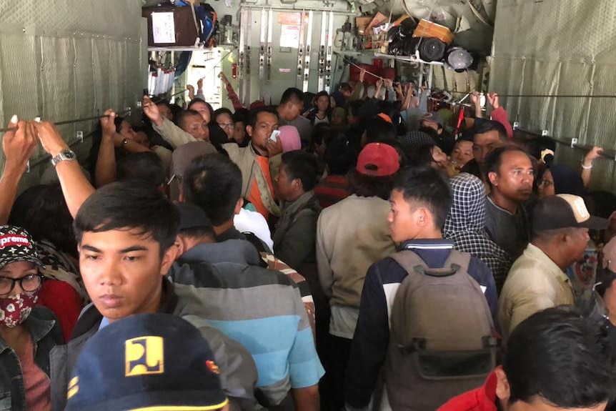 A large crowd stands inside a military aircraft