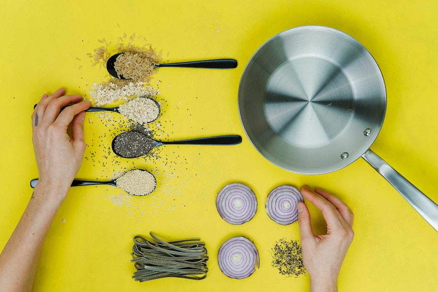 Overhead photo of fry pan, grains, pasta, sliced onion and hands about to cook, depicting ways to kick start your savings.