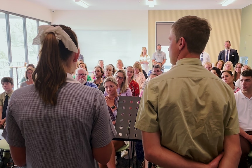 Two students speak to a room full of students in the audience.