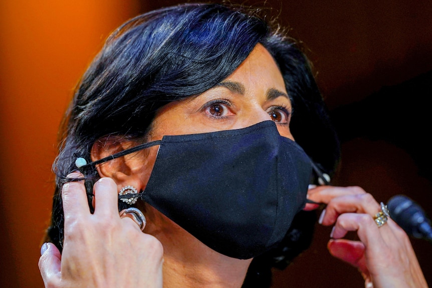 A woman putting on a black face mask