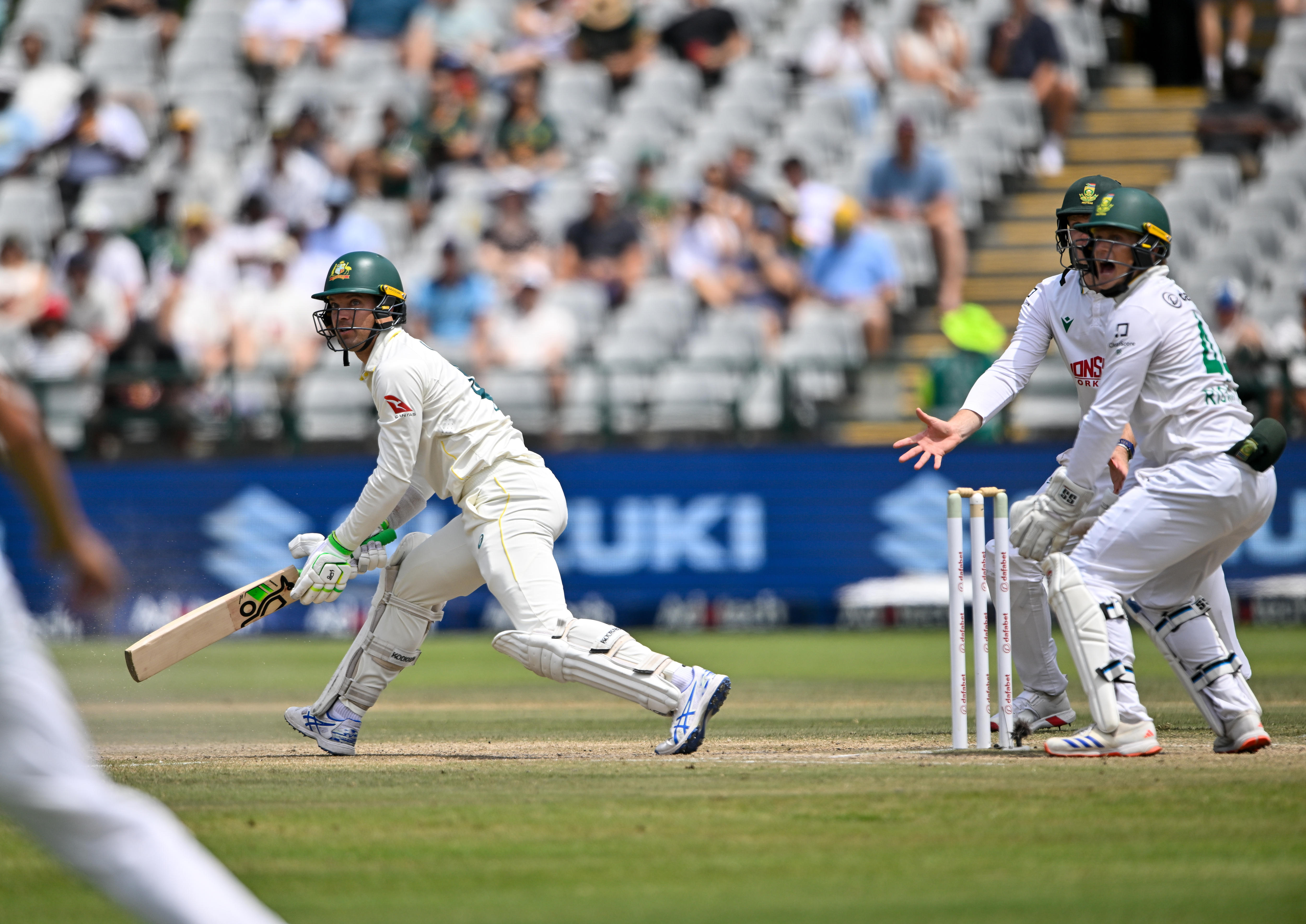 A cricket batter plays a shot with wicketkeeper behind him