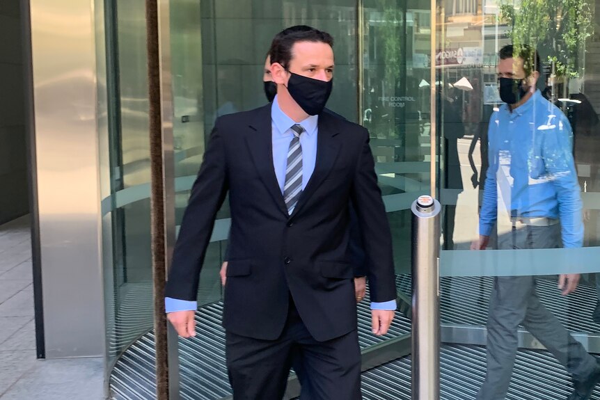 A man wearing suit and tie and a face mask walks out of a building.