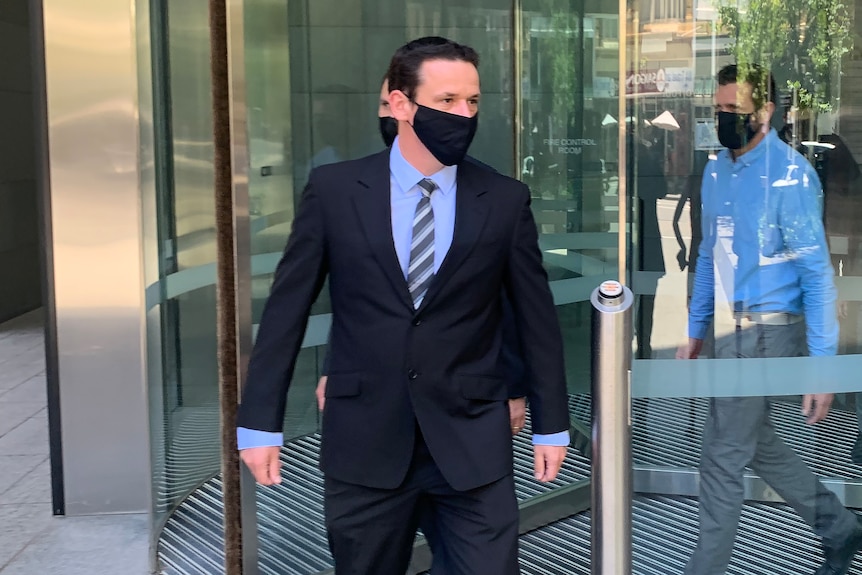 A man wearing suit and tie and a face mask walks out of a building.