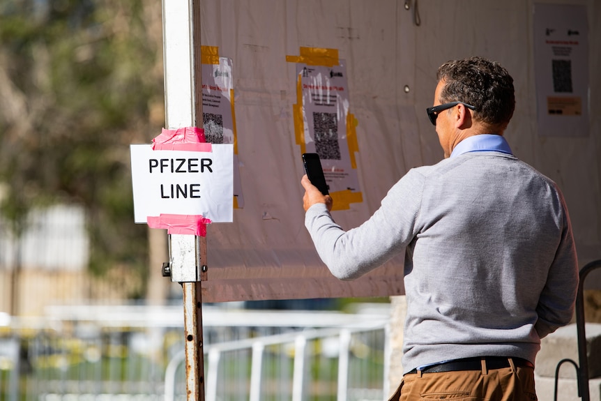 A man scanning a QR code next to a sign that reads' Pfizer Line'.