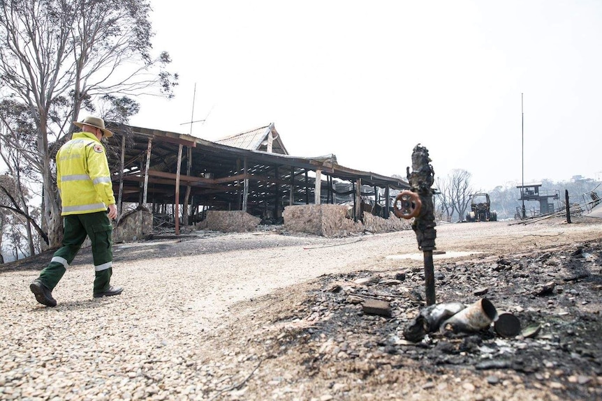 A park ranger passes the burnt out shell of a ski chalet, with the remnants of trucks and chairlifts visible in the distance.