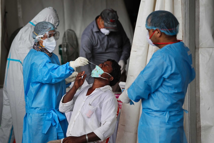 Health workers conduct COVID-19 antigen tests for a male patient in New Delhi, India